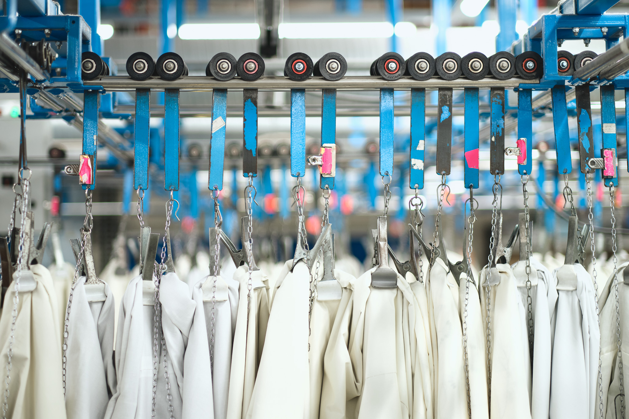 Rows of white garments hanging on metal hangers and chains, suspended from a blue automated conveyor system at Standfast & Barracks.